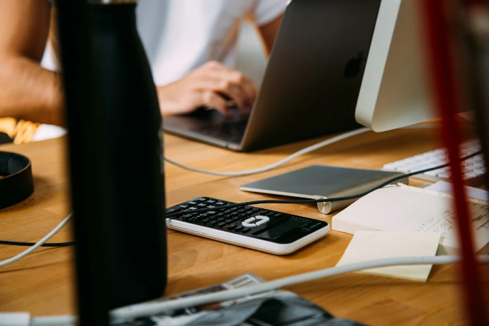 A professional education consultant working at a clean office desk with a laptop and notebooks, focused on analyzing school system data and instructional reports.
